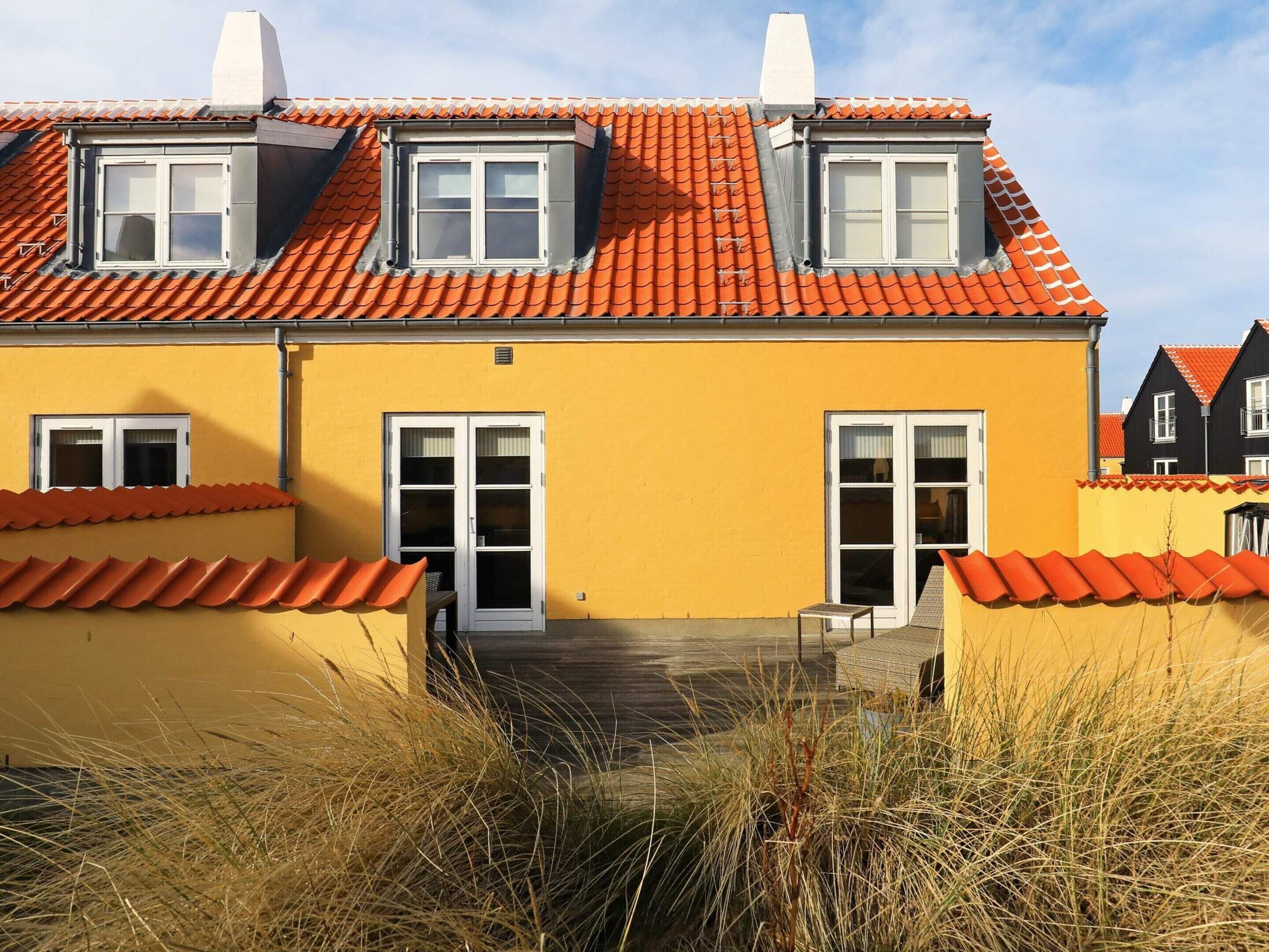 A yellow building with a red-tiled roof, two dormer windows, and a central door.