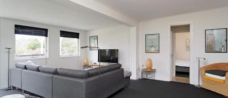 A modern living room with a grey sectional sofa, a flat-screen TV, and a small table with a lamp.