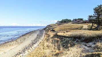 A coastal landscape with a pebble beach, grassy terrain, and a clear sky.