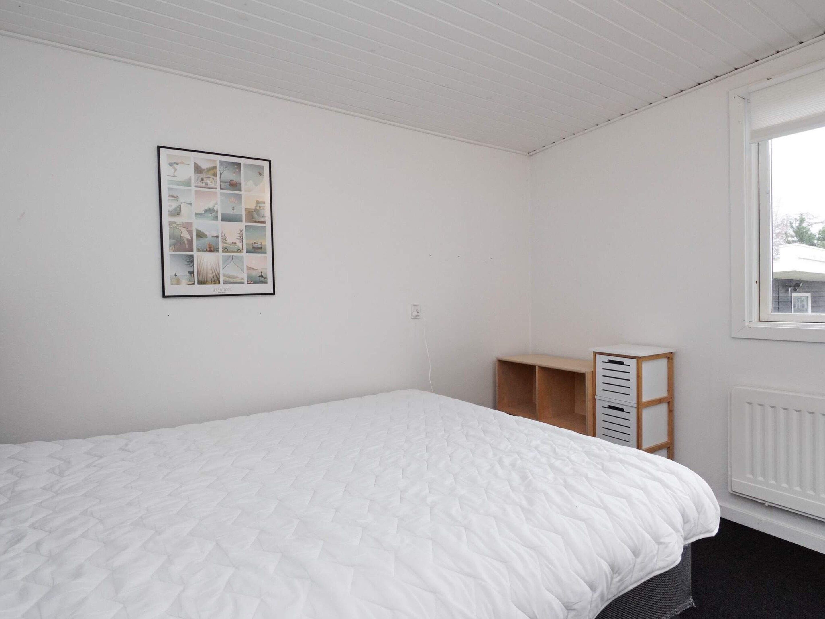 A bedroom with a bed, a framed picture on the wall, a window, and a radiator.