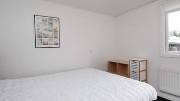 A bedroom with a bed, a framed picture on the wall, a window, and a radiator.
