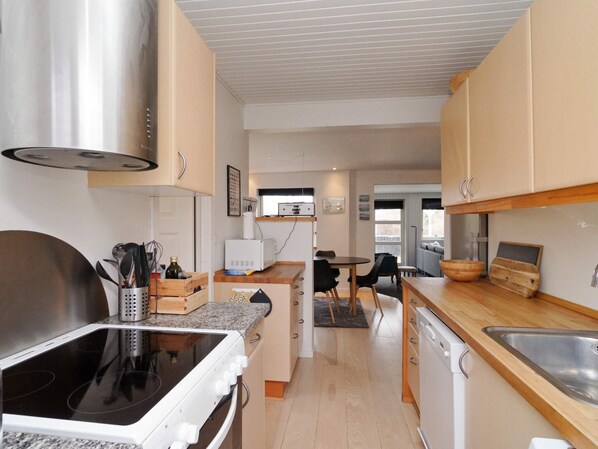 A modern kitchen with a stove, microwave, and dishwasher. There is a dining area with a table and chairs. - 5 Person Holiday Home in Gilleleje (Gilleleje)