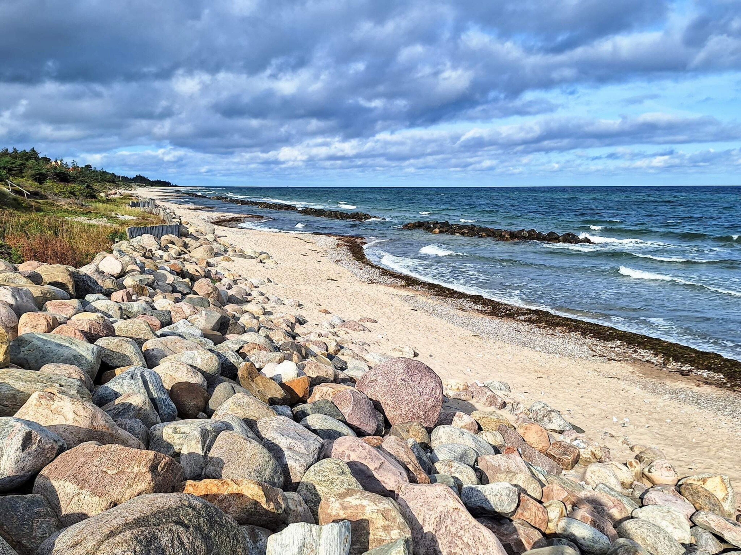 A rocky beach with waves, a clear sky, and distant hills.