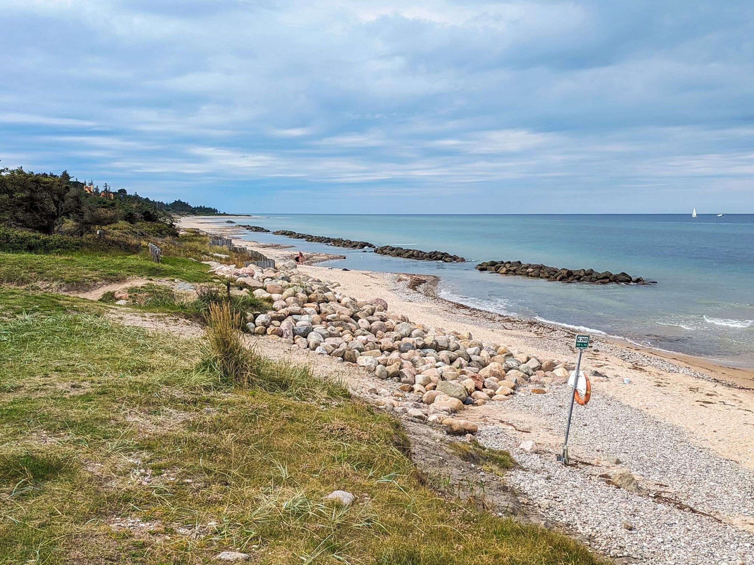 A coastal beach with a rocky shoreline, a lifebuoy, and a clear sky.