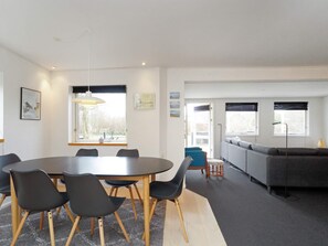 A modern living room with a dining area, featuring a round table, chairs, a sofa, and a large window with blinds. - 5 Person Holiday Home in Gilleleje (Gilleleje)
