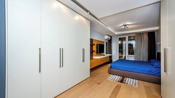 A modern bedroom with a large bed, a wardrobe, a desk, and a television.