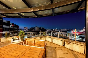 A rooftop terrace with a view of a city skyline at dusk.