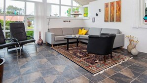 A modern living room with a grey sofa, black armchairs, a patterned rug, and large windows.