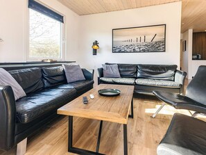 En moderne stue med en sort lædersofa, et træbord og en sort lænestol. Et sort-hvidt fotografi hænger på væggen.