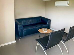 A small room with a black leather sofa, a round wooden table with two chairs, and a wall-mounted air conditioner. - 4 Star Holiday Home in Albaek (Aalbaek)