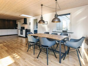 A modern kitchen with wooden cabinets, a built-in oven, and a dining area with a wooden table and blue chairs.