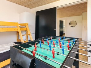 Une pièce avec une table de baby-foot, un lit superposé et une porte qui donne sur une autre pièce.