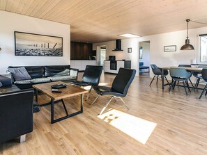 A modern living room with a wooden floor, black leather sofa, and a dining area with a table and chairs.