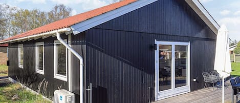 A black metal building with a red roof, a wooden deck, and a sliding glass door.