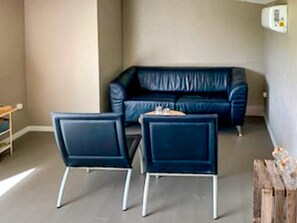 A room with a dark blue leather sofa, two matching armchairs, a small wooden table, and a white wall-mounted heater.