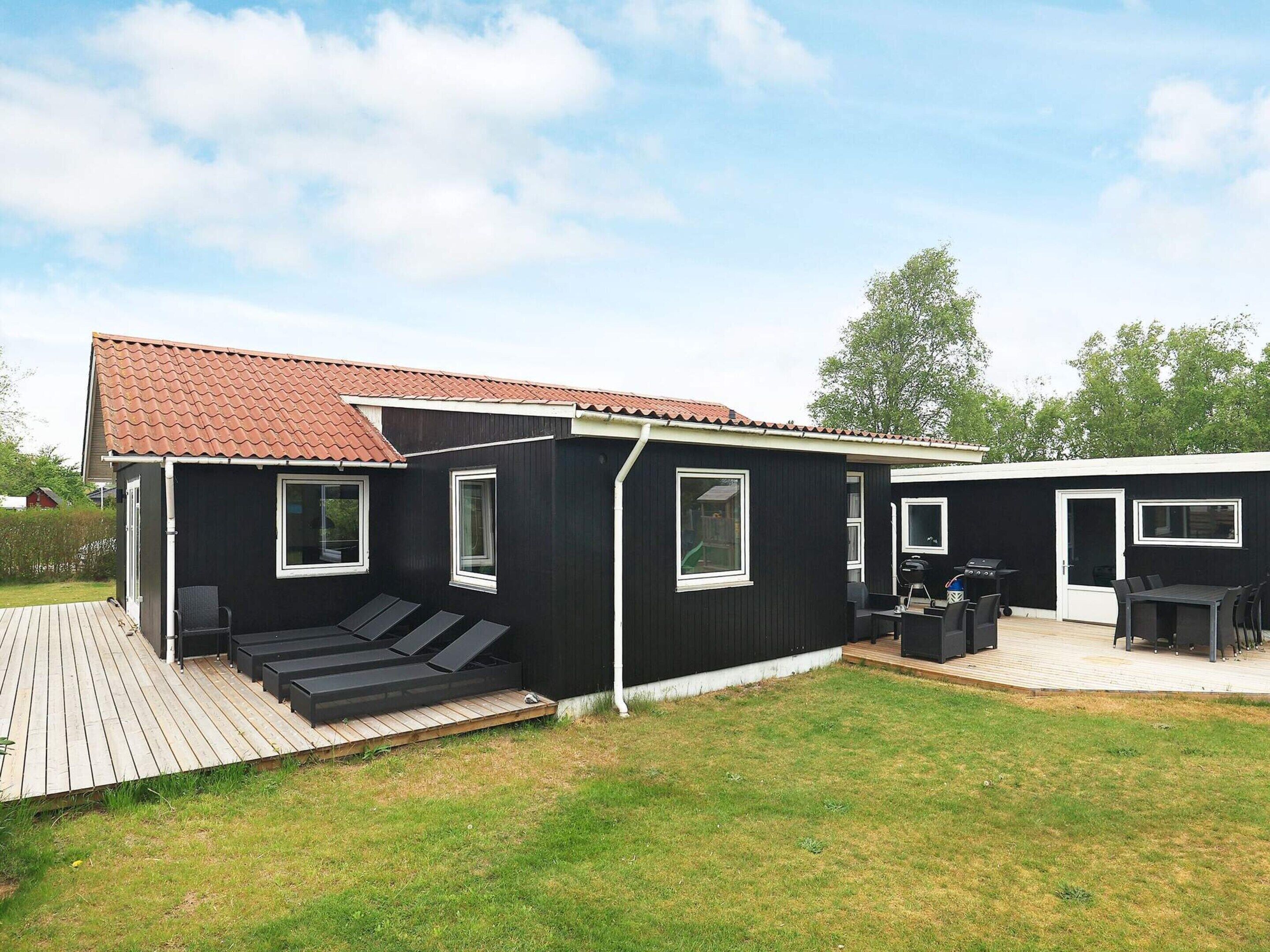 A modern black house with a red-tiled roof, a deck, and a patio area with outdoor furniture.