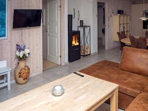 A living room with a sofa, a TV mounted on the wall, a fireplace, and a vase with flowers on a table. - 6 Person Holiday Home in Hurup Thy (Hurup Thy)