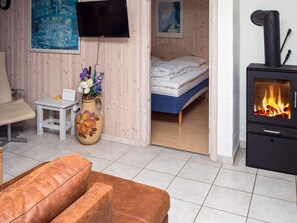 A cozy room with a bed, a small table with a vase of flowers, a sofa, a television, and a wood-burning stove. - 6 Person Holiday Home in Hurup Thy (Hurup Thy)