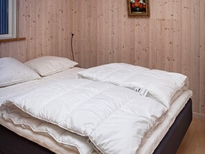 Een netjes opgemaakt bed met witte beddengoed in een kamer met houten paneelwanden.
