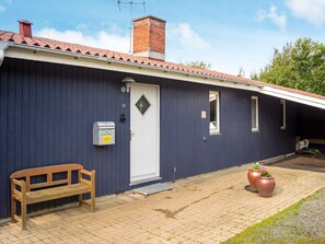 A building with a dark blue exterior, a white door, a small window, a mailbox, and a wooden bench.