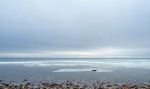 A beach with pebbles and a calm sea under a cloudy sky.