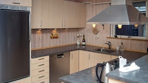 Eine moderne Küche mit einem Edelstahl-Kühlschrank, Holzschränken, einem eingebauten Geschirrspüler und einer großen Kochinsel mit Wasserkocher und Kaffeemaschine.