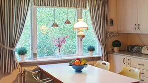 Un coin repas comprenant une table, des chaises, un panier de fruits et une fenêtre avec des rideaux.