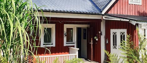 A red wooden house with a dark roof, white windows, and a porch with a white railing.