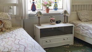 Une chambre avec deux lits, une table de chevet, une fenêtre ornée de petites figurines décoratives et une vue sur la verdure à l’extérieur.