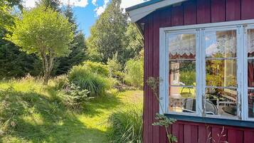 A red wooden building with a window overlooking a garden.