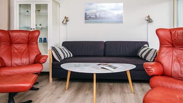 Ein Zimmer mit einem dunkelgrauen Sofa, zwei roten Ledersesseln, einem kleinen weißen Tisch und einer Vitrine mit Glastüren.