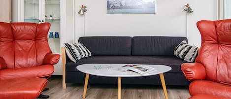 A room with a dark grey sofa, two red leather chairs, a small white table, and a cabinet with glass doors.