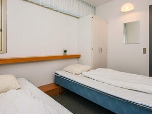 Ett sovrum med två enkelsängar, en trähylla med en växt, en garderob, en spegel och en lampa.