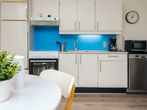 A compact kitchen with white cabinets, a blue backsplash, a microwave, a coffee maker, and a dishwasher. - 4 Person Holiday Home in Ringkobing (Ringkobing)