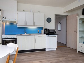A compact kitchen with white cabinets, a blue backsplash, a microwave, a coffee maker, and a clock on the wall.
