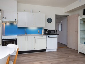 A compact kitchen with white cabinets, a blue backsplash, a microwave, a coffee maker, and a clock on the wall.