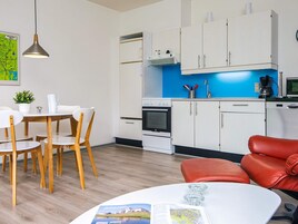 Una cucina moderna con mobili bianchi, un piano cottura e un forno a microonde. C'è una zona pranzo con tavolo e sedie, e un divano in pelle rossa.