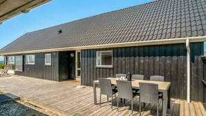 Une terrasse en bois avec une table et des chaises, un espace couvert et un bâtiment doté d’un toit en tuiles.