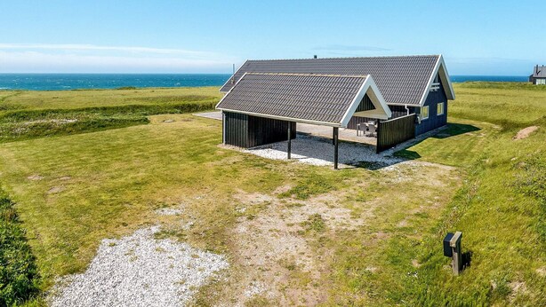 Une maison moderne avec un toit en pente, un espace extérieur couvert et une vue sur la mer.