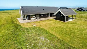 Une maison de plain-pied dotée d’une grande terrasse, d’un garage séparé et offrant une vue sur la mer.