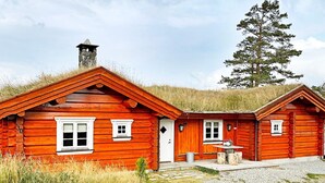 Une cabane en rondins avec une cheminée, deux fenêtres et un petit porche.