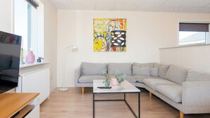 A modern living room with a grey sofa, a coffee table, and a TV on a wooden stand. - 14 Person Holiday Home in Ringkobing (Ringkobing)