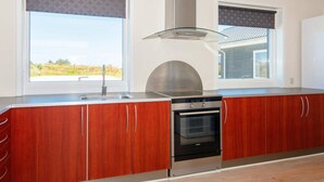 A modern kitchen with wooden cabinets, a stainless steel range hood, and a built-in oven. - 14 Person Holiday Home in Ringkobing (Ringkobing)