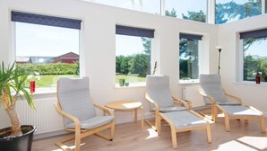 A sunlit room with three wooden-framed chairs and a small table, large windows with dark blinds, and a potted plant. - 14 Person Holiday Home in Ringkobing (Ringkobing)