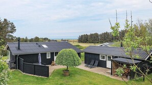 Une rangée de petites cabanes aux couleurs sombres, surmontées de toits en métal, disposées côte à côte, avec un espace herbeux au milieu.