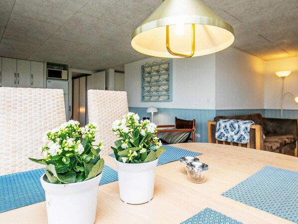 A dining area with a round table, two potted plants, and a hanging light fixture.