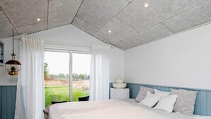 Une chambre avec un grand lit, une table de chevet avec une lampe et une vue sur un espace verdoyant par la fenêtre.