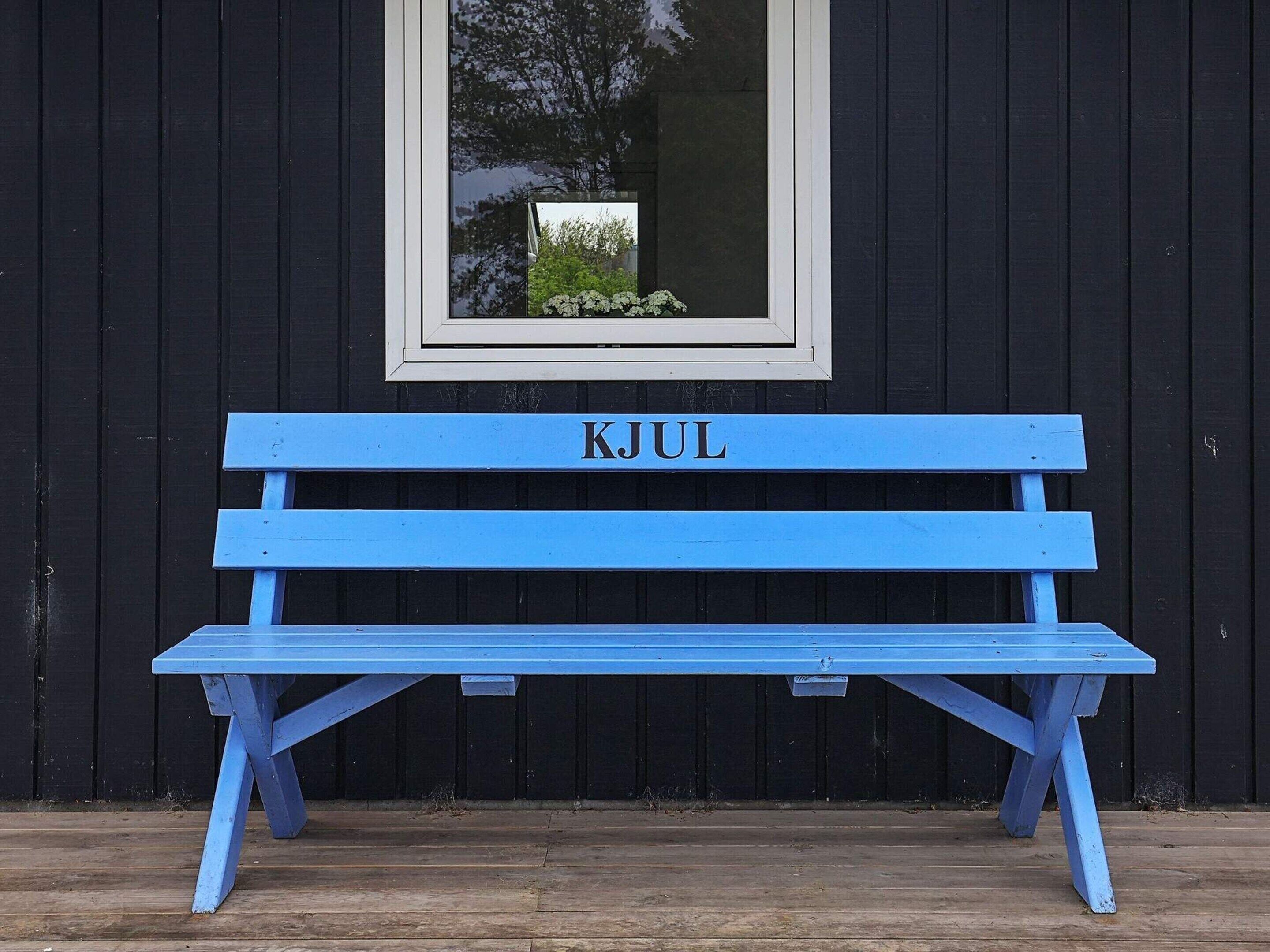 Un banc bleu portant l’inscription « KJUL », le tout sur un fond en bois noir.