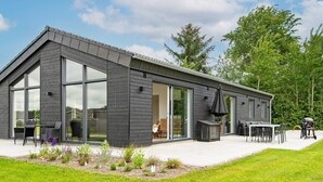 Una casa moderna con amplios ventanales correderos, un patio con mobiliario exterior y un césped bien cuidado.