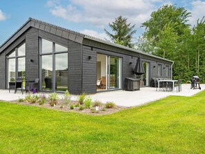Et moderne hus med store skydedøre, en terrasse med udendørs møbler og en velplejet græsplæne.